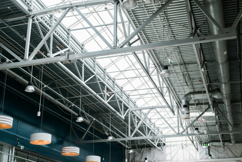 Nexel Electric | Electrical Services | Metal roof structure of a large building, indoors. Built-in windows at the top for lighting